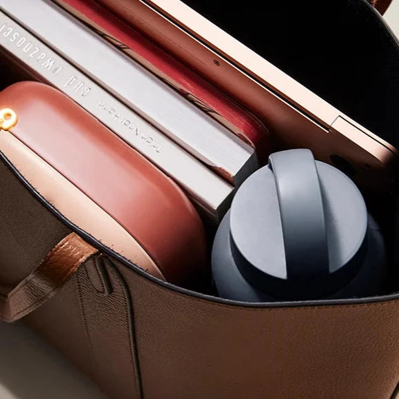 grijze drinkfles in tas met laptop, boeken, en bakje.