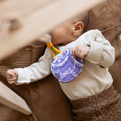 Baby met lila smiley speenkoord en een leopard broekje aan en een beige romper aan