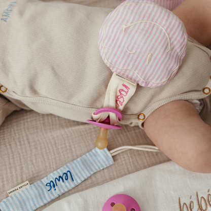 Roze-wit gestreept speenkoord van linnen, met een vrolijke witte smiley knuffel, perfect als origineel cadeau voor een pasgeborene.