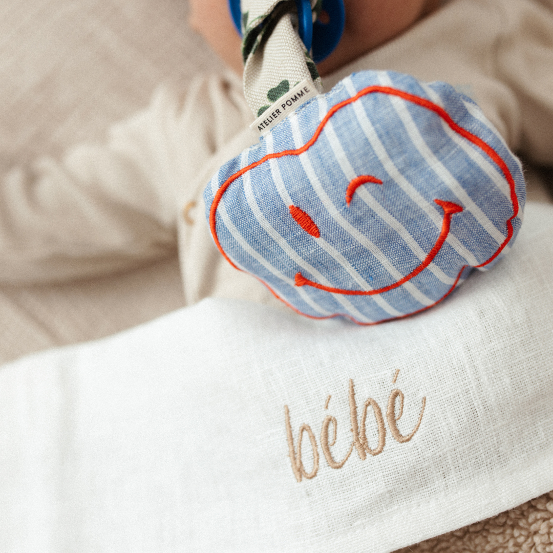 peenkoord met een klavertjesontwerp en een smiley knuffel met blauwe strepen en een rood geborduurde lach, perfect als baby shower cadeau