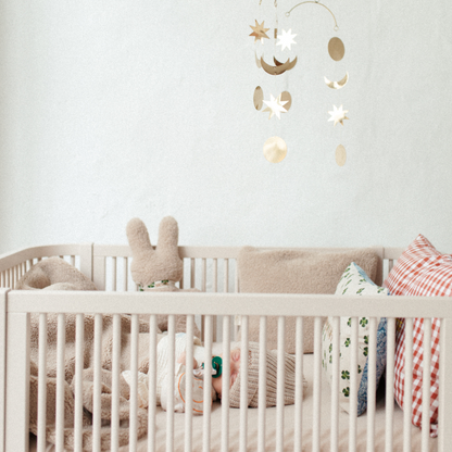 baby ligt in ledikant met knuffel, teddy deken en kussens. 