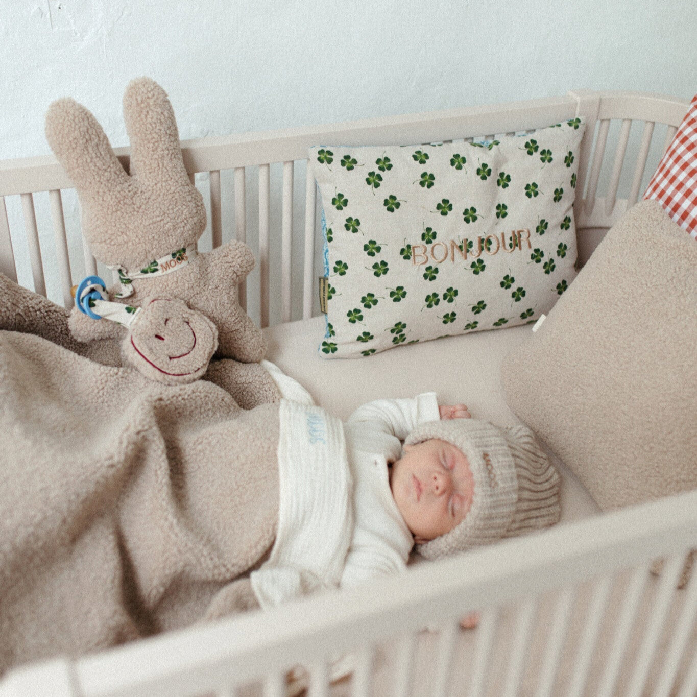 baby ligt in ledikant onder teddy dekbedset, kussens met tekst, speen met speenkoord, teddy knuffel. 