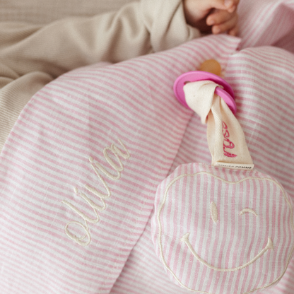 baby ligt onder gestreept laken met tekst. speen met gestreept speenkoord