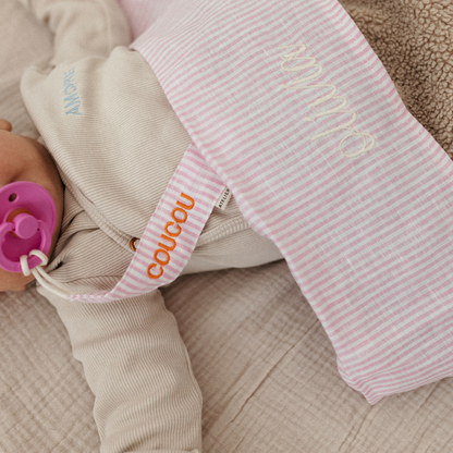 baby ligt onder gestreept laken met tekst en speen met speenkoord
