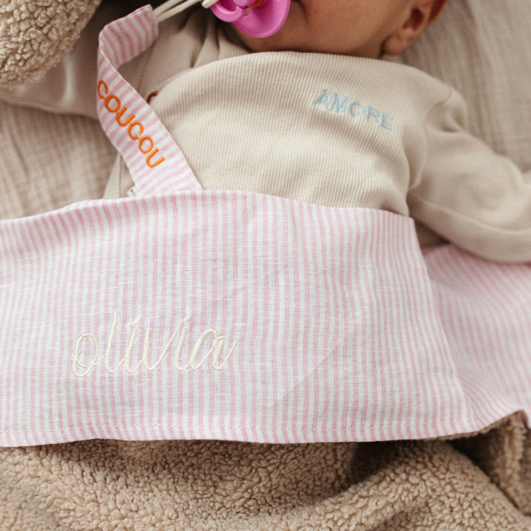 baby ligt onder gestreept laken met tekst. knuffel, speen, speenkoord met tekst. 