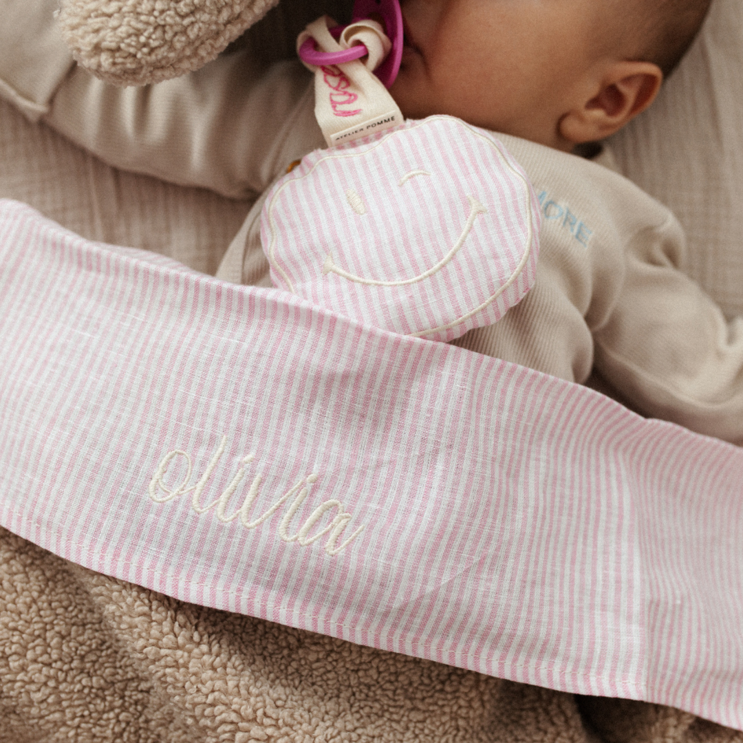 baby ligt onder gestreept laken met tekst. knuffel, speen, gestreept speenkoord met tekst. 