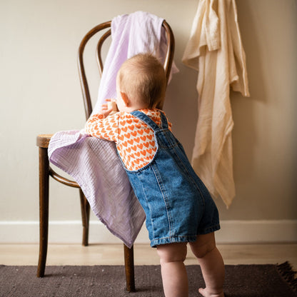 baby leunt tegen stoel met daaroverheen een laken 