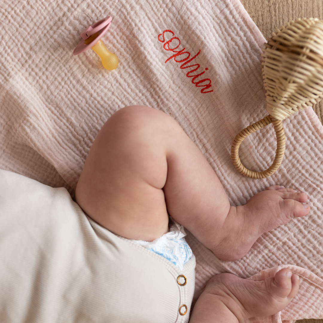 baby ligt op gepersonaliseerd laken met speen en rammelaar