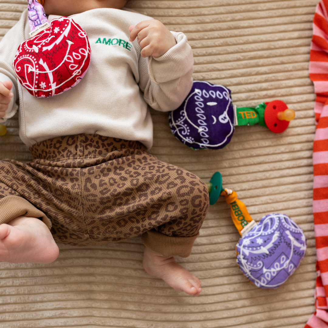 baby ligt met speen en speendoekje in de mond. met daarnaast speen en speenkoorden met tekst. 