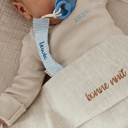 baby ligt onder laken met gepersonaliseerde tekst en speenkoord met tekst 