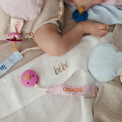 baby ligt op laken met tekst, spenen met speenkoorden en speenknuffels met tekst