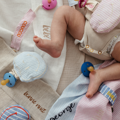 baby ligt op laken met tekst, spenen met speenkoorden en speenknuffels met tekst