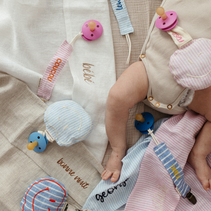 baby ligt op laken met tekst, spenen met speenknuffels en speenkoorden met tekst