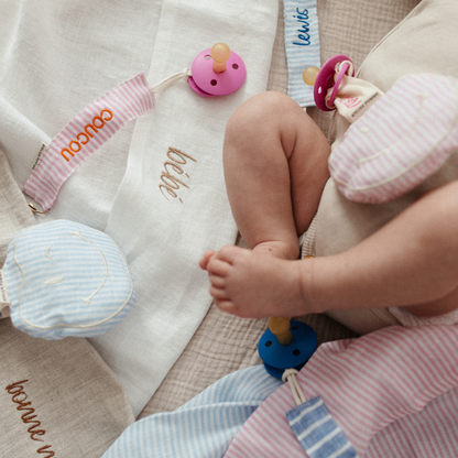 baby ligt op laken met tekst, spenen met speenknuffels en speenkoorden met tekst
