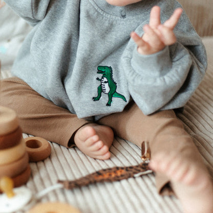 baby speelt met houten speelgoed en draagt grijze sweater met icoon 