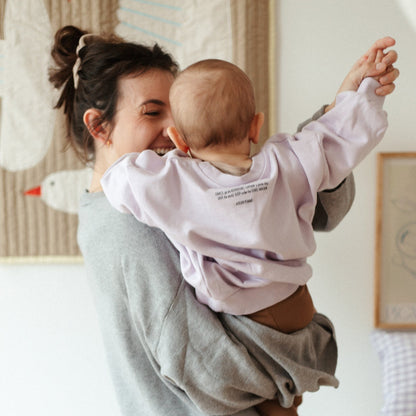 baby draagt lila sweater en wordt gedragen door vrouw. 