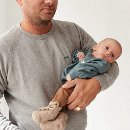 baby draagt een blauwe sweater en wordt vastgehouden door man. 