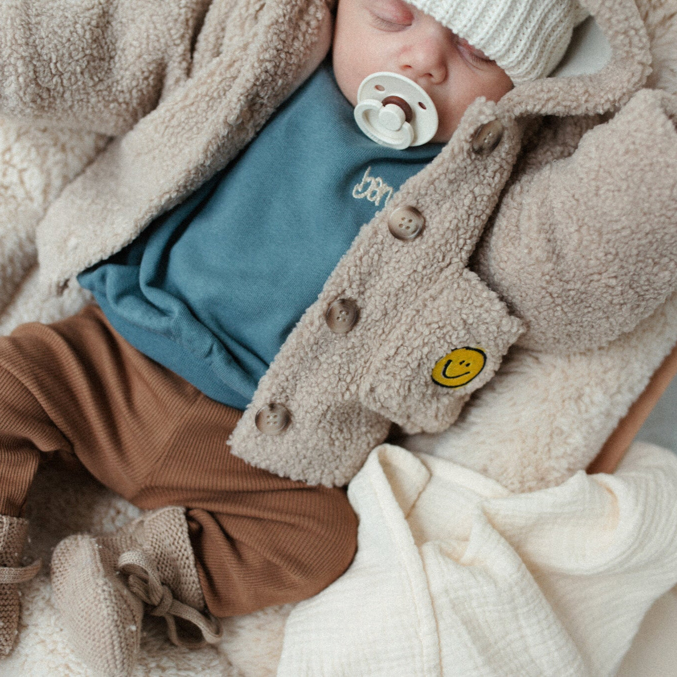 baby draagt blauwe sweater en teddy jasje. 