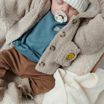 baby draagt blauwe sweater en teddy jasje. 