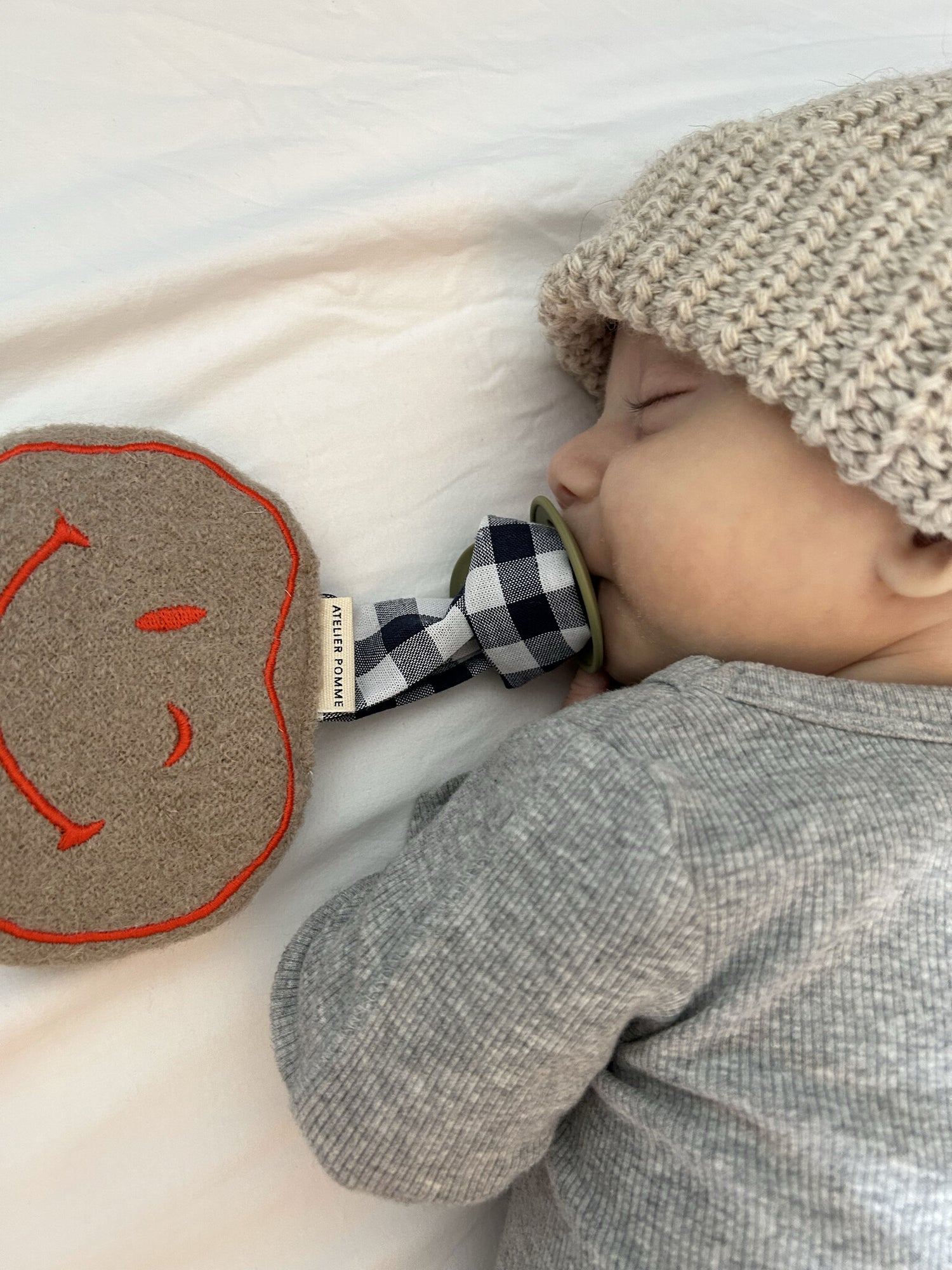 Smiley knuffel speenkoord van zachte wollen stof met een oranje smiley, met een geruit koord om een speen aan te bevestigen.