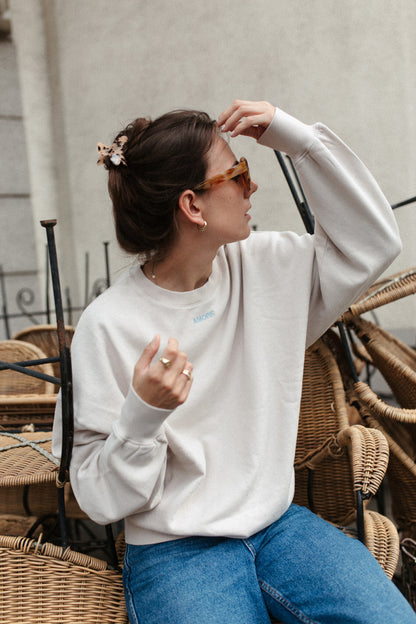 Moeder en vrouw in een oversized beige sweater. Gepersonaliseerd met amore in licht blauw. Gemaakt van 100% biologisch katoen.