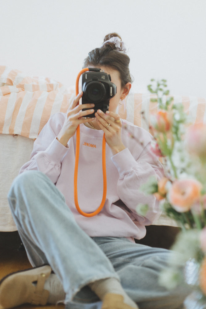 Vrouw in oversized lila trui met personalisatie van quote in oranje. Leuk voor op een spijkerbroek. 