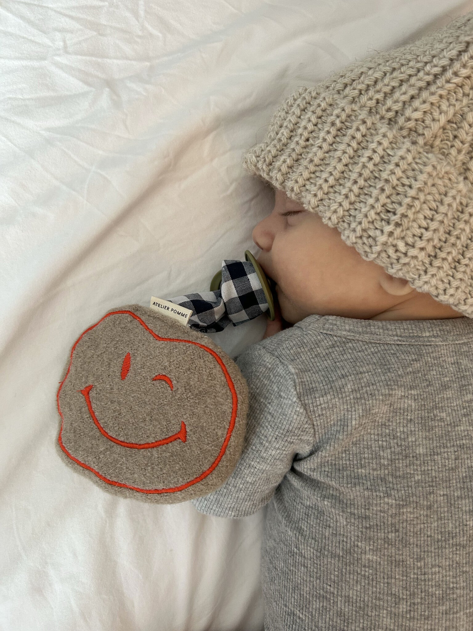 baby met speenkoord met geruit patroon een wollen smiley.