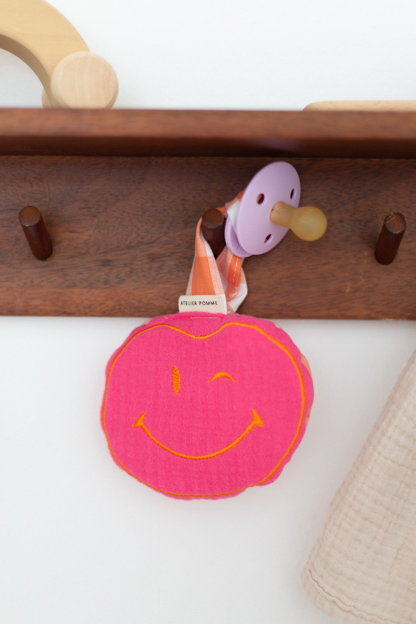 Handgemaakte roze en oranje smiley knuffel aan een geruit speenkoord, een kleurrijk en praktisch accessoire voor baby&