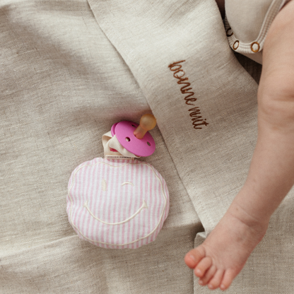 Roze-wit linnen speenkoord met een schattige witte smiley knuffel, ideaal als baby shower cadeau.